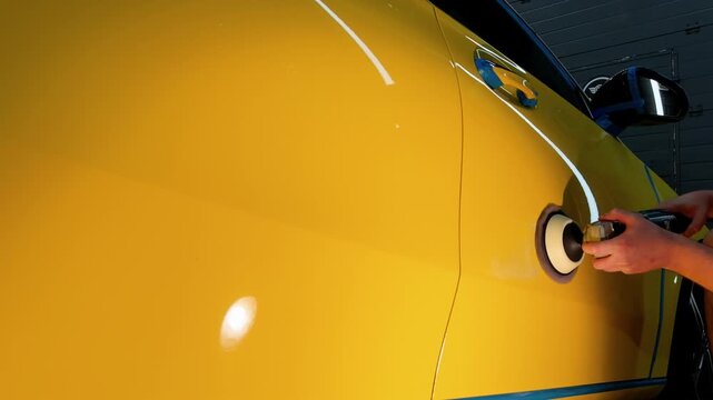 A car service worker polishes the yellow car body with a polishing machine. Detailing and polishing of the car. Car detailing - hands with an orbital polishing machine in an auto repair shop. PDR. 