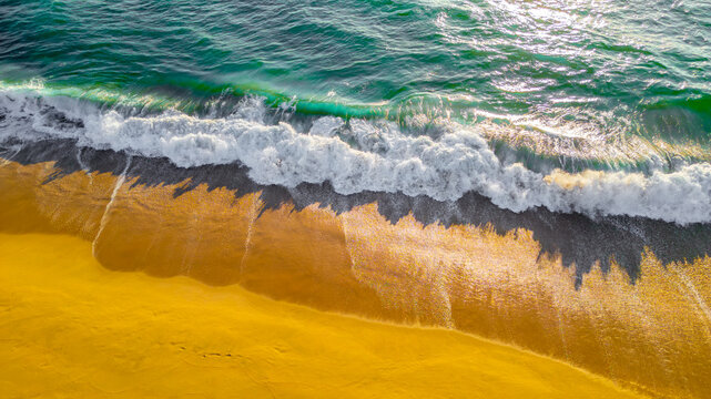 Aerial view of the golden sandy beach and turquoise Pacific Ocean waves crashing onto the shore in Todos Santos, Baja California Sur, Mexico.