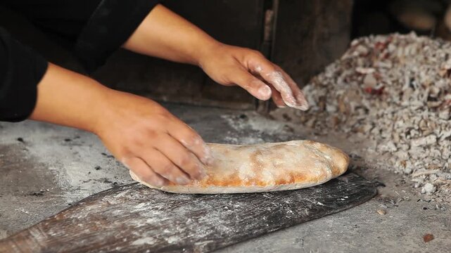 Freshly baked bread from a traditional stone oven being split in two by a person. Authentic village life and traditional culinary culture.