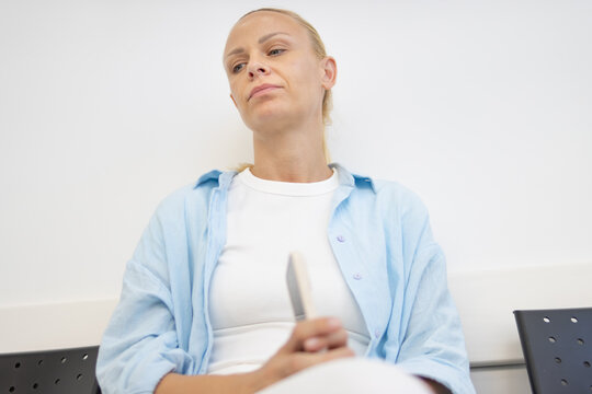 Woman experiencing anxiety and boredom while waiting for an appointment in a hospital or clinic, feeling sad and disappointed about the situation