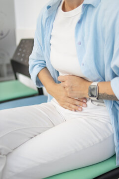 Woman suffering from severe abdominal pain and cramps, touching her stomach with both hands, experiencing discomfort, sickness, and needing relief from a health issue