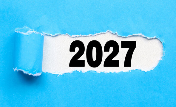 Torn blue paper revealing the year 2027 underneath. Happy new year 2027 lettering reveal through tornado paper. Happy New Year coming concept.