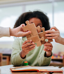 Diverse students hands connecting wooden jigsaw puzzle pieces together on desk during classroom activity within school building © Lahmz