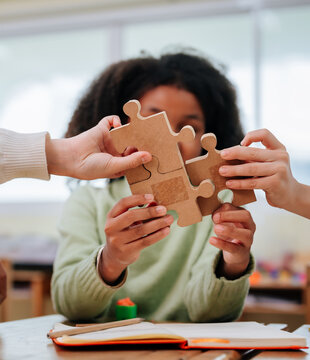 Diverse students hands connecting wooden jigsaw puzzle pieces together on desk during classroom activity within school building
