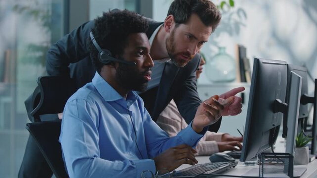 Diversity business team man with woman working in call center Caucasian boss coming helping with advice pointing in computer talk to African American businessman in callcenter office hotline helpline