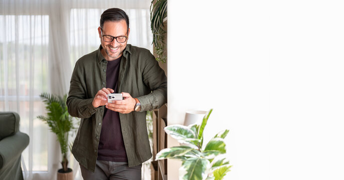 Man in casual clothing smiling while using a cellphone, exploring applications, and interacting online, showcasing concepts of connectivity and modern lifestyle