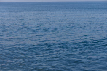 Naklejka premium Calm blue sea stretches endlessly under a clear sky with gentle waves lapping at the shore