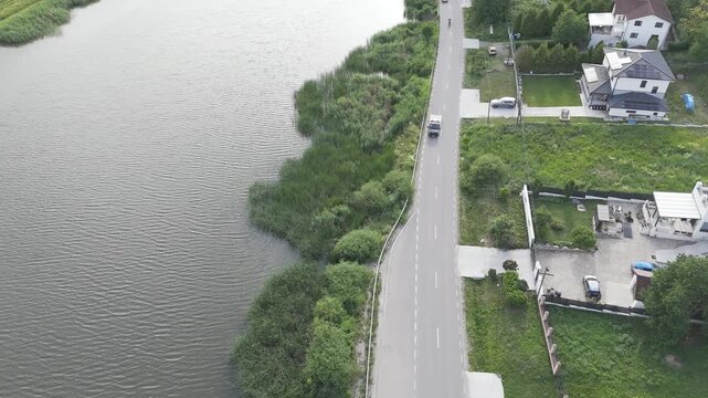 Drone Aerial Bird's Eye View with Lake on the Left and Parallel Countryside Road on the Right, Following the Scenic Waterfront Shoreline and Rural Infrastructure from Above