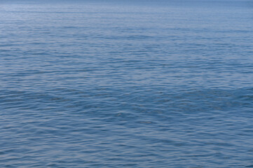 Obraz premium Calm waves gently lap against the shore at a tranquil seaside location in midday sunlight