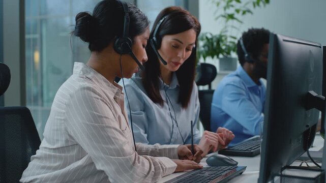 Three multiracial business coworkers team working in call center. Caucasian woman intern asking help with corporate software talking with African American female helping showing thumb up in callcenter