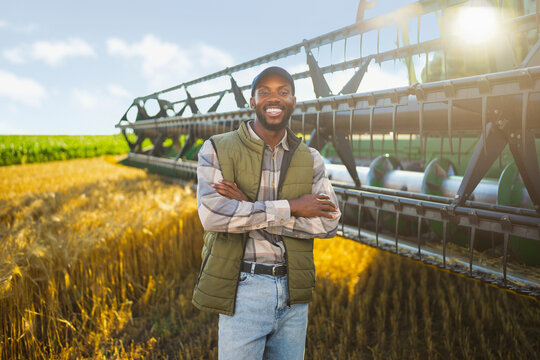 Smiling farmer standing beside harvesting equipment during a successful wheat harvest.