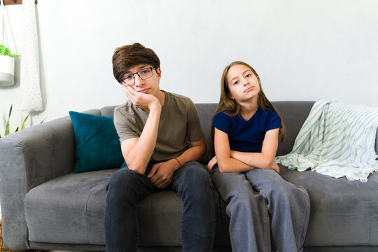 Bored siblings sitting on couch at home, feeling upset and having nothing to do during childhood
