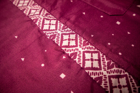 Detailed close-up showing the intricate traditional Indonesian batik patterned placket on a maroon fabric shirt