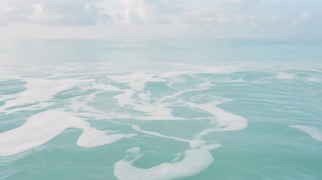 Calm ocean waves gently flowing under a soft cloudy sky with serene turquoise water