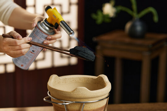 Lighting charcoal with a butane torch over a clay brazier indoors