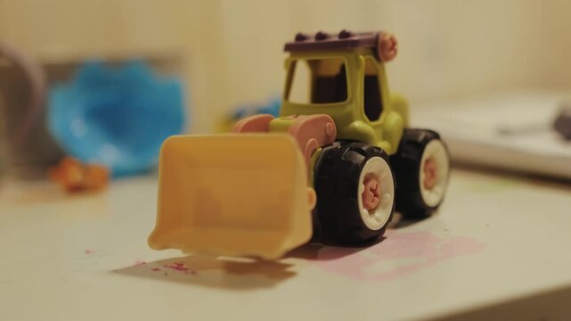 Colorful toy tractor displayed on a table in children room with scattered toys and warm light