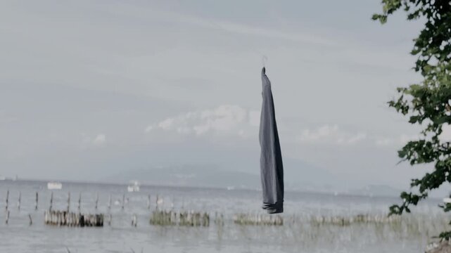 Dark grey long sleeve shirt hanging sideways on a hanger in front of a calm coastal sea landscape