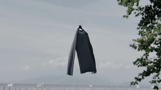 Grey long sleeve crewneck shirt hanging on a hanger against an open sea and cloudy sky background