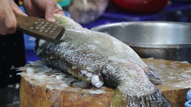 Street Food Vendor Descaling Fresh Fish on a Wooden Cutting Board