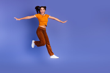 Joyful young female teen jumps in a stylish casual outfit against a purple background for lifestyle...