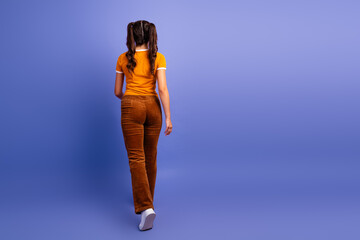 Naklejka premium Young female teen model walks away on a purple studio backdrop showcasing casual fashion lifestyle and a playful mood