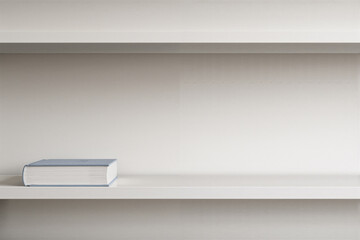 Fototapeta premium Single closed book lying on empty white shelf in minimalist room with minimalist, background