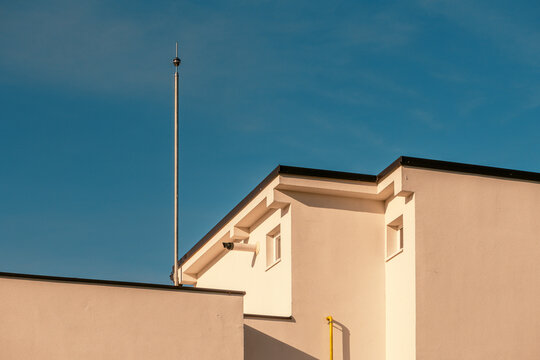 Minimalist residential building facade with lightning rod in warm sunlight, clean geometric architecture against deep blue sky