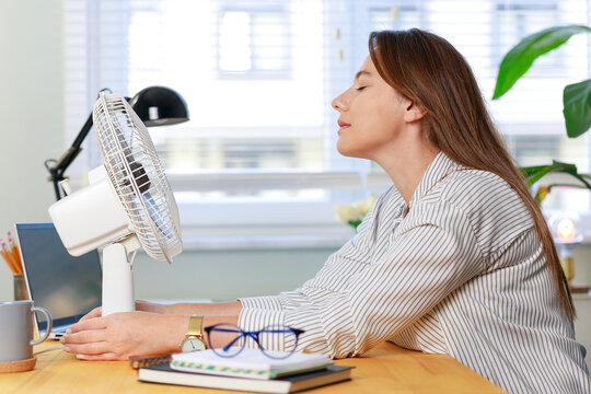 Woman cooling herself with desk fan during hot weather