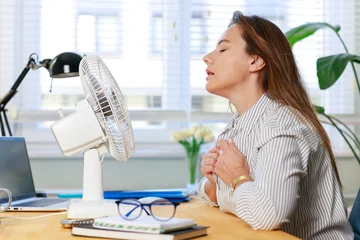 Fototapeten Restaurant Woman cooling herself with desk fan during hot weather  © dragonstock