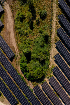 Aerial view of rows of solar panels arranged in a field with a central patch of green vegetation and dirt paths in Saint-Denis-de-l'Hotel, Centre-Val de Loire, France.