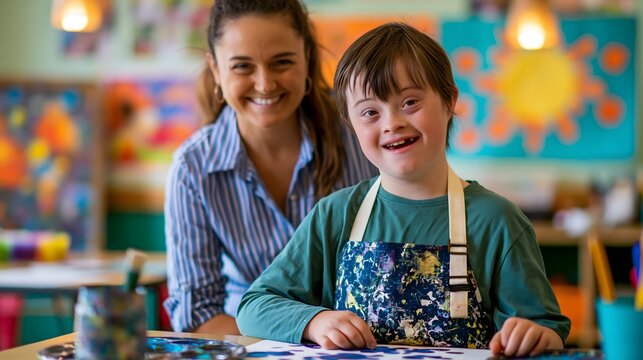 Portrait of mixed race boy age 8 with Down syndrome wearing apron doing art project in inclusive classroom. Joyful smile, teacher behind him. Warm lighting. Down syndrome awareness, inclusive educatio
