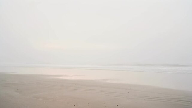 Calm empty beach with soft sand and gentle waves under a hazy sky at sunrise or sunset