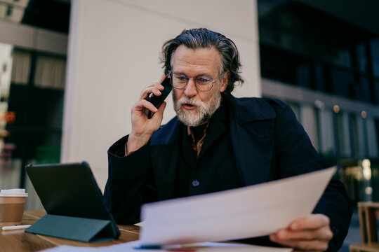 Wide shot of successful mature professional with digital tablet sitting at outdoor workspace near modern office building, copy space, digital nomad lifestyle, financial freedom, career growth.