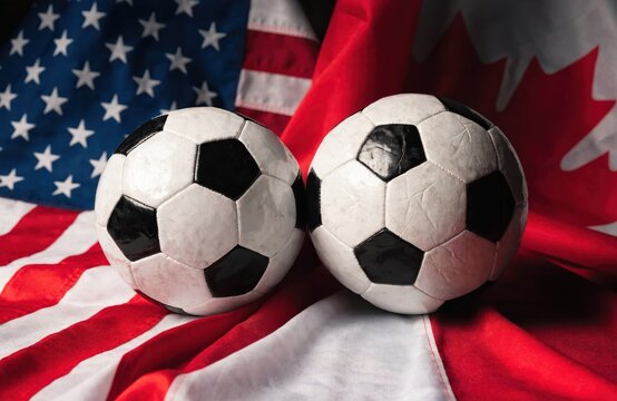 Two Soccer Balls Resting on United States and Canada Flags Representing North American Football Competition