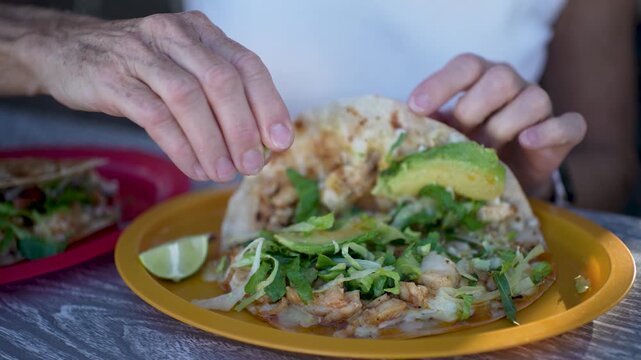 Senior woman smiles while squeezing lime on tasty fish and shrimp tacos at a taco stand in Baja California Mexico
