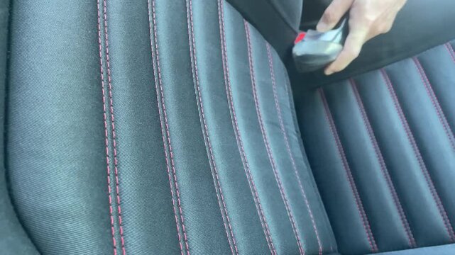 Close up horizontal shot of a person vacuuming a black fabric car seat with red stitching using a wet extraction machine nozzle during a professional detailing process. High quality 4k footage