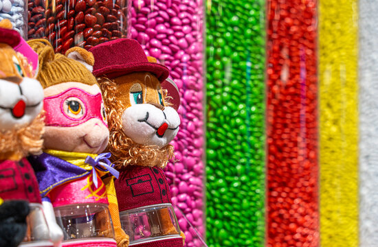 Cute Stuffed Animal Plush Toys Standing in Front of Vertical Tubes Filled with Colorful Candies