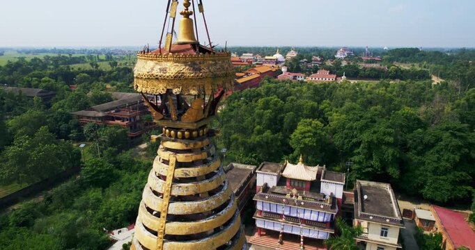 Aerial close-up of a white stupa topped with a golden spire, overlooking colorful temples and green forest in the Lumbini monastic zone, Nepal.
