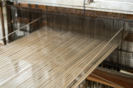 Close up view of stretched warp threads on a traditional wooden handloom. Indonesian authentic tenun fabric production workshop.