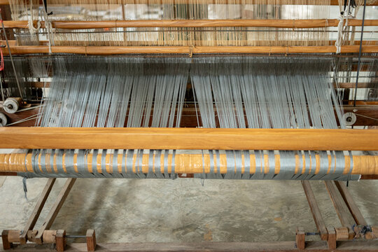 Front view of fine blueish grey warp threads stretched across a traditional wooden handloom. Authentic Indonesian tenun textile production process.