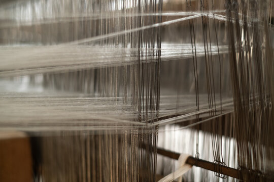 Macro detail of intersecting warp threads and heddle strings on a traditional weaving loom. Intricate Indonesian authentic tenun fabric craftsmanship.
