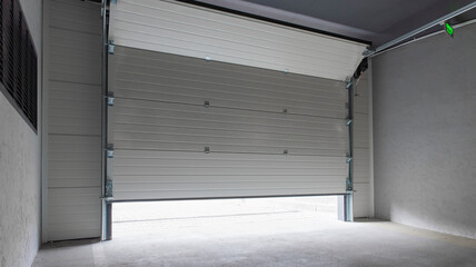 Fototapeta premium Partially open white automatic sectional garage door in underground parking