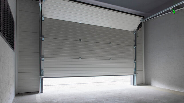 Partially open white automatic sectional garage door in underground parking