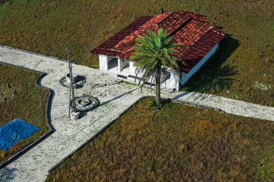 Aerial view of Kuda miskih mosque with a red tiled roof, a palm tree, and a white sandy path surrounded by a grassy cemetery with grave markers in Makunudhoo, Haa Dhaalu Atoll, Maldives.