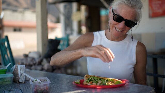 Senior woman smiles while adding toppings to her quesataco at a taco stand in Baja California Sur during her trip