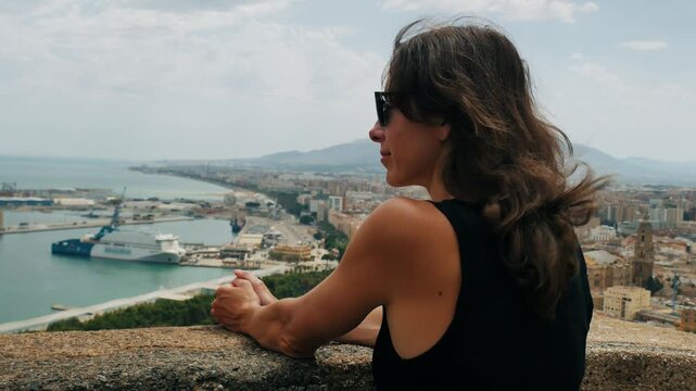 Woman embracing panoramic Malaga cityscape with calm contemplation, embodying freedom and self-discovery on a sunny urban coast.