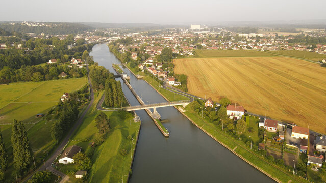 Aerial view of the canal lock and bridge surrounded by fields, trees, and residential houses in Pontoise, Ile-de-France, France.
