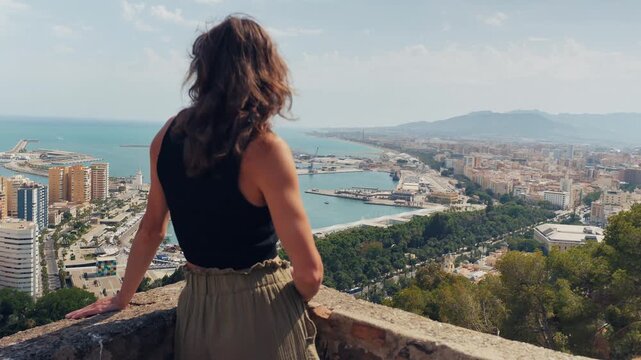 Woman embracing panoramic Malaga cityscape with calm introspection, embodying solo wanderlust and mental wellness in a stunning urban retreat.