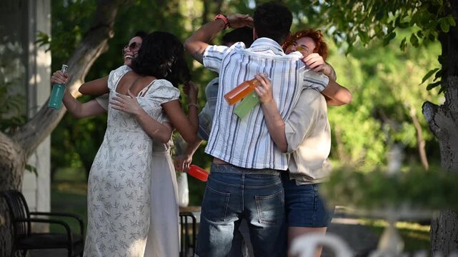 Friends reunite, hug, and dance at an outdoor summer party, celebrating with drinks amid a lush garden