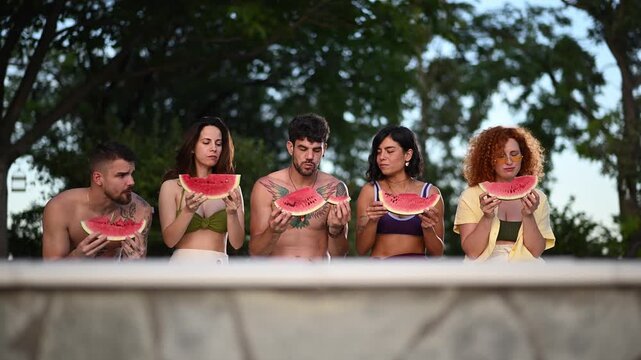 Group of happy young friends eating fresh watermelon slices outdoors enjoying a summer snack together